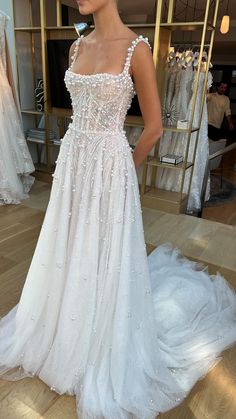 a woman standing in front of a dress on display at a bridal shop wearing a white gown with beaded detailing