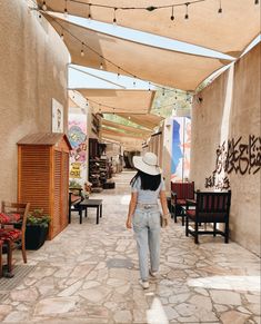 a woman walking down an alley way with lots of tables and chairs on either side