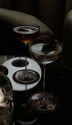 three martini glasses sitting on top of a table next to a glass filled with liquid