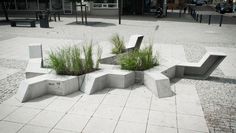 three cement benches with plants growing out of them on a sidewalk in front of buildings