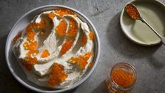 a white bowl filled with cream and orange toppings next to two spoons on a table