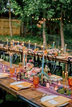 a long table with candles, plates and napkins is set for an outdoor dinner