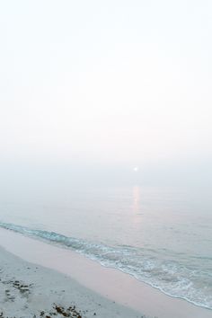 an empty beach with the ocean in the background and foggy skies above it on a hazy day