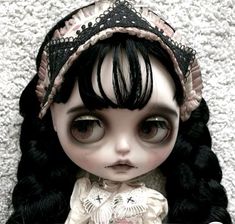 a doll with long black hair wearing a dress and headband on top of a white carpet