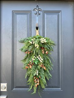 a wreath hanging on the front door of a house decorated with greenery and pine cones