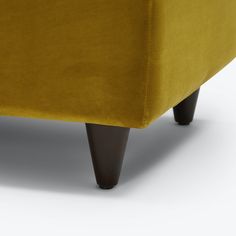 an upholstered couch with wooden legs and a mustard colored velvet finish, viewed from the front