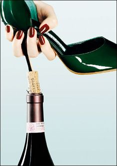 a woman's hand holding a wine bottle with a green shoe on top of it