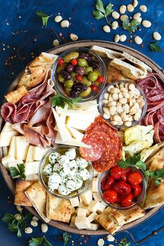 a platter filled with meats, cheeses and other foods on a blue surface