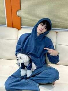 a person sitting on a couch with a small white dog in their lap and wearing a blue hoodie