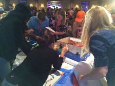 a group of people standing around a table with boxes on top of it and papers in front of them