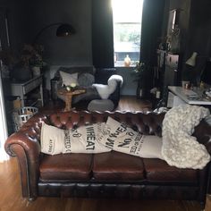 a brown leather couch sitting in a living room next to a chair and table with two pillows on it