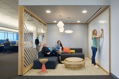 three people are sitting on couches in an office with glass partitions to the wall