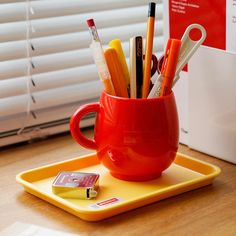 a red cup filled with pens and pencils on top of a yellow tray