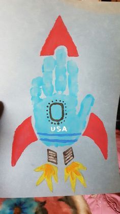 a child's hand holding up a sign with a rocket ship painted on it