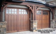 two wooden garage doors in front of a brick building with stone pillars and arched windows