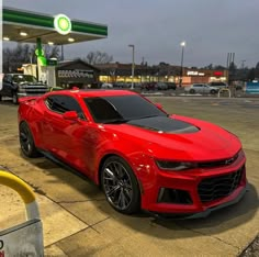 a red chevrolet camaro parked in front of a gas station