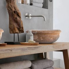 a wooden table topped with a bowl filled with lots of soap next to a wall mounted towel dispenser