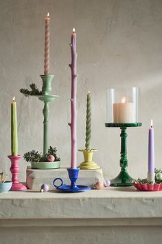 there are many candles on the table and one candle is pink, green, blue, yellow