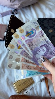 a person is holding money in their hand on a bed with other items around them