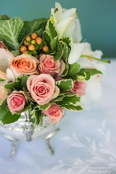 a vase filled with pink and white flowers on top of a table next to green leaves