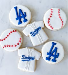 four decorated cookies in the shape of shirts and baseballs, one with dodgers on it