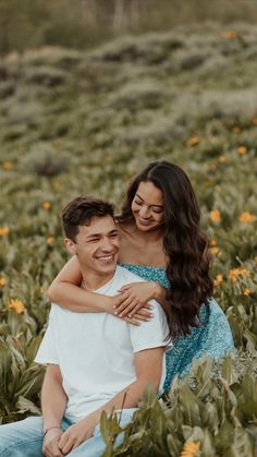 a man and woman sitting in the middle of a field full of flowers smiling at each other