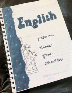 an open notebook with the words english written in blue and white on it, next to a statue of liberty