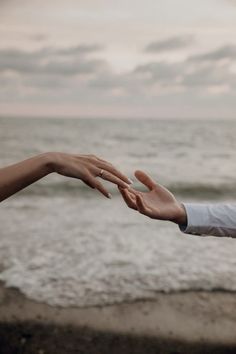 two people reaching out their hands to touch each other on the beach with waves in the background