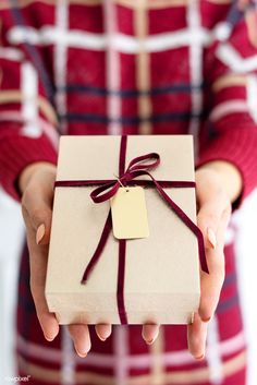 a person holding a wrapped gift box with a tag on it's side and a red ribbon around the top