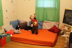 a young boy standing on top of an orange bed in a room with green curtains