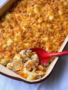 a casserole dish filled with macaroni and cheese, topped with a red spoon