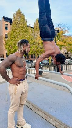 two men doing tricks on skateboards in front of a railing with one man upside down