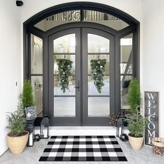 the front door is decorated with potted plants and two wreaths on each side