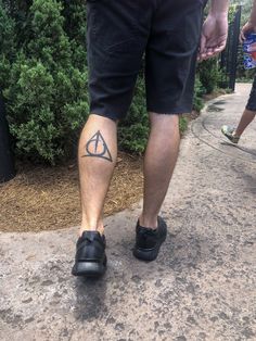 a man with a tattoo on his leg walking down a sidewalk in front of some bushes