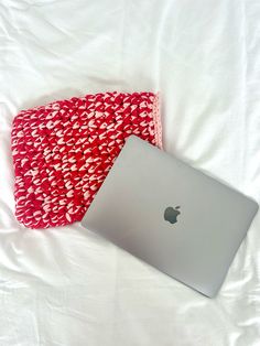 an apple laptop computer sitting on top of a white bed next to a red and white blanket