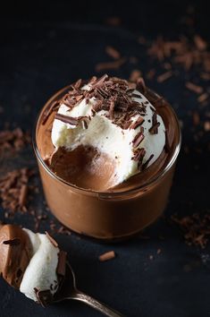 a chocolate dessert with whipped cream and chocolate shavings on the side, next to a spoon