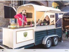 a man and woman standing at the back of a food truck with bottles on it