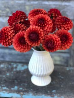 a white vase filled with red flowers on top of a table