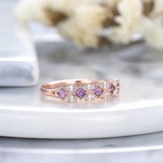 a pink diamond ring sitting on top of a white marble table next to some flowers