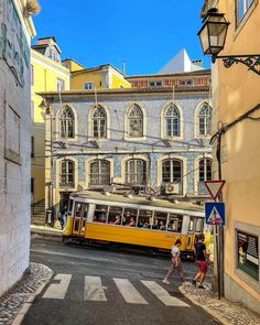 a yellow trolley is going down the street in front of some buildings and people walking by