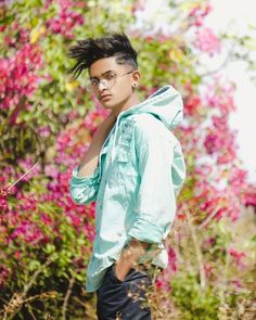 a young man with black hair and glasses standing in front of pink flowers