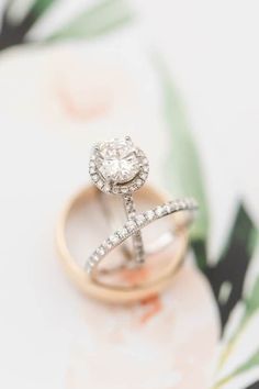 two wedding rings sitting on top of each other in front of a flowery background