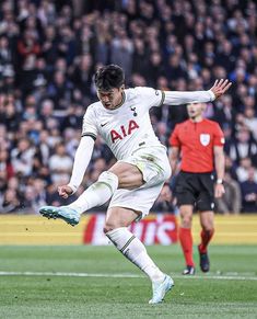 a man kicking a soccer ball on top of a field next to other people in the stands