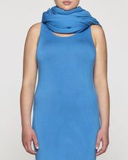 a woman wearing a blue dress with a cowl neck and sleeveless top, standing in front of a white background