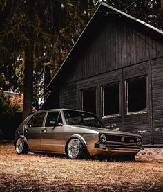 an old car parked in front of a wooden building with trees and grass around it