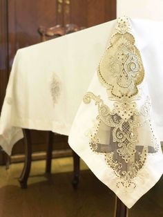 a white table cloth with an ornate cross on it and a wooden chair in the background