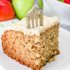 a piece of cake on a plate with a fork stuck in it and some apples behind it