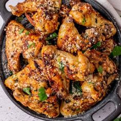 a skillet filled with chicken wings covered in parmesan cheese and cilantro