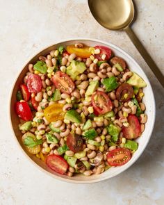 a white bowl filled with beans, tomatoes and avocado next to a spoon