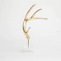 a gold sculpture of a bird on a clear stand against a white background in the shape of an antelope